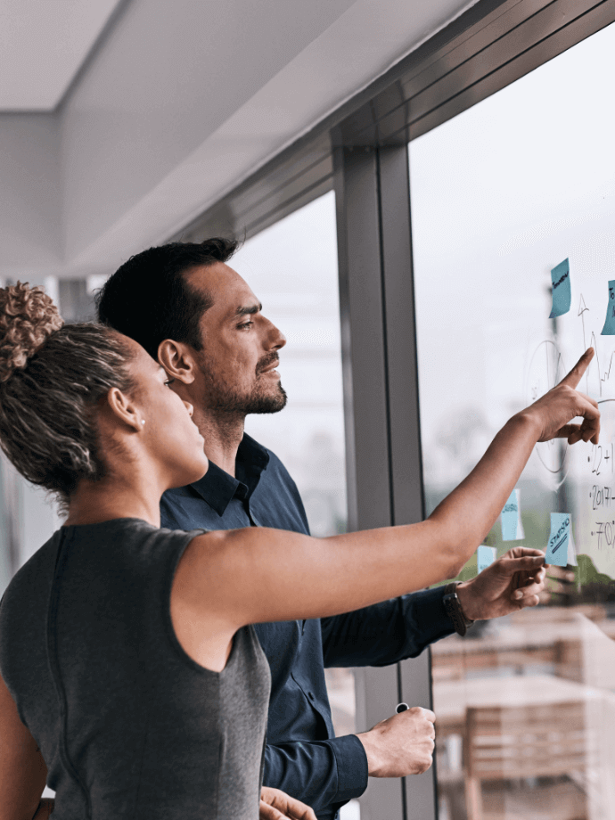 a couple of business people observing a graph and numbers on a glass wall